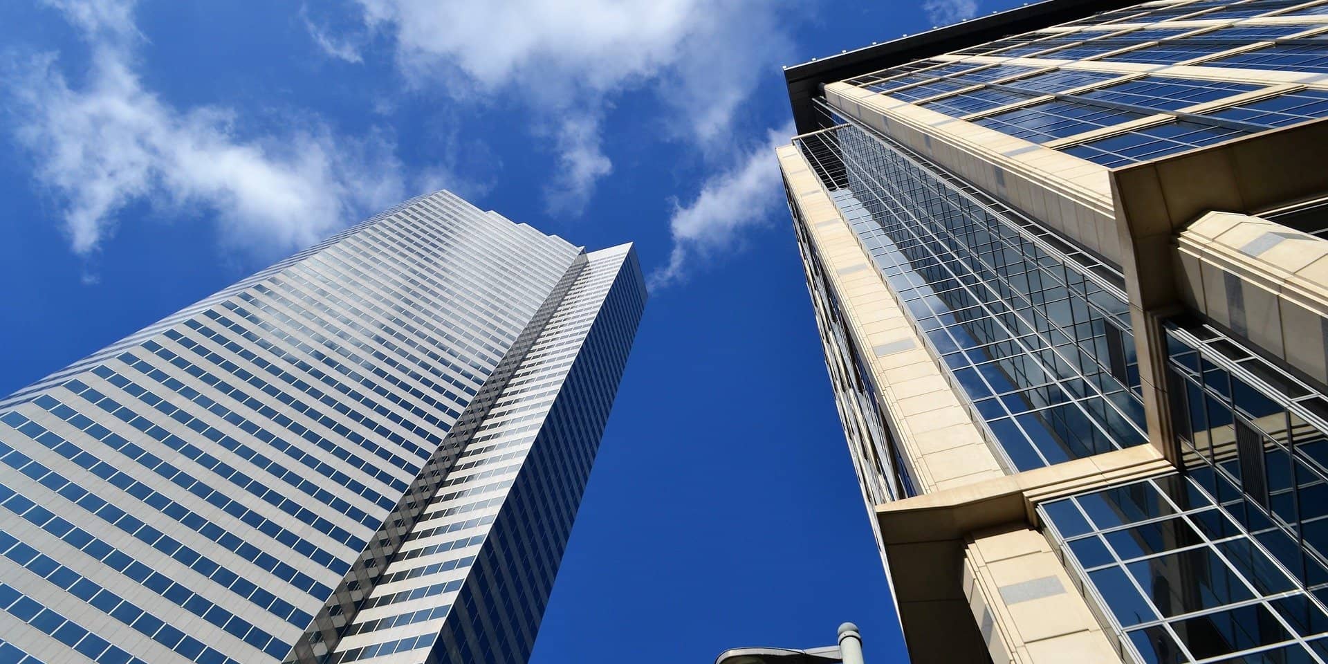 Two modern skyscrapers extending into a clear blue sky, with industrial solar panels visible on the glass facade of the building on the right.