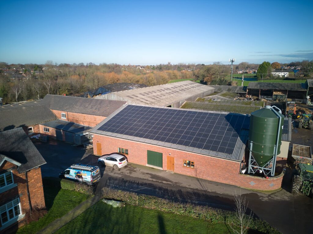 Aerial view of a farm with buildings equipped with commercial solar PV by scasolar, a storage silo, a white car, and a truck parked beside.