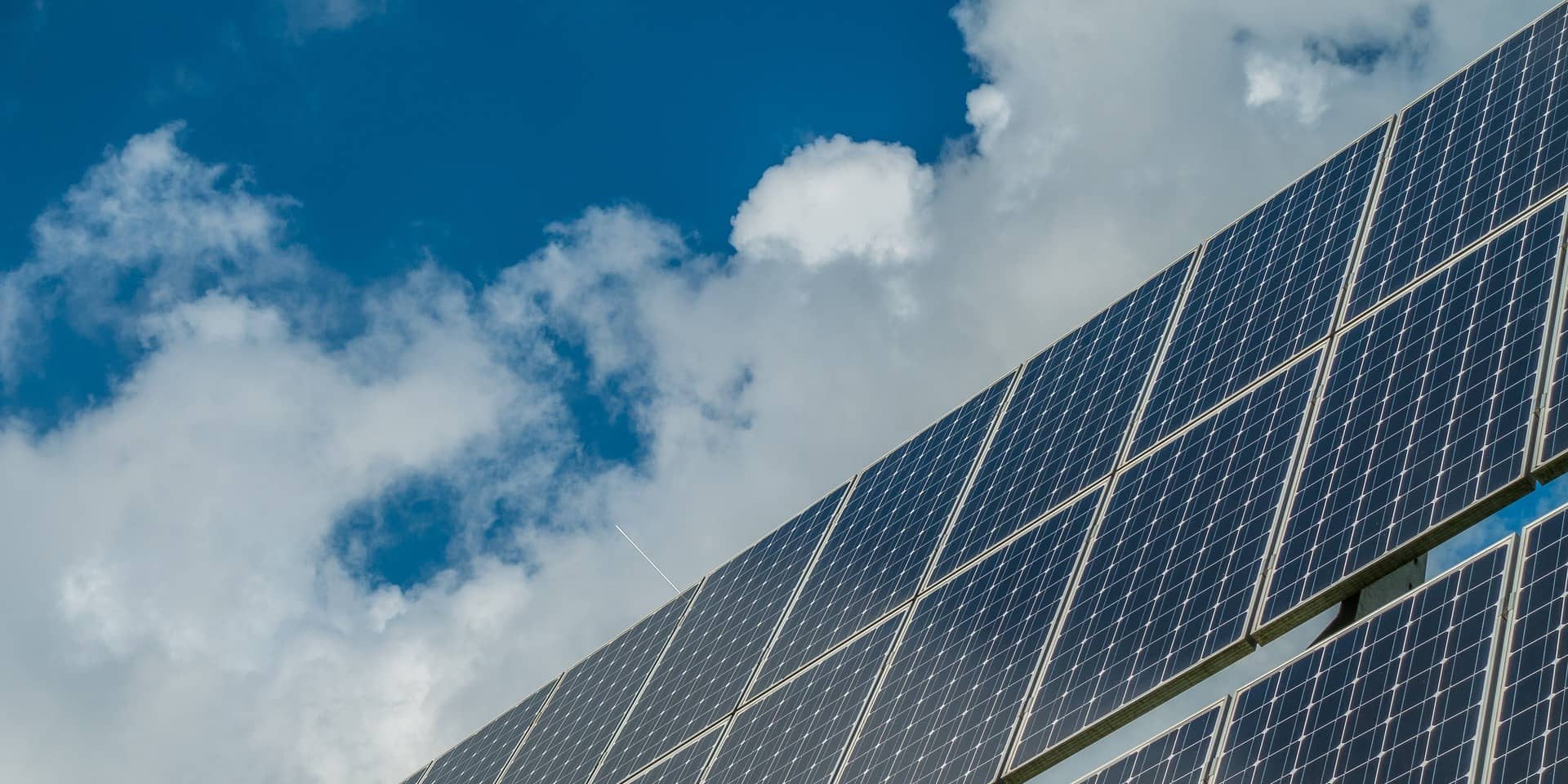 Solar panels against a blue sky with fluffy clouds, highlighting renewable energy technology as a solution to rising energy prices.