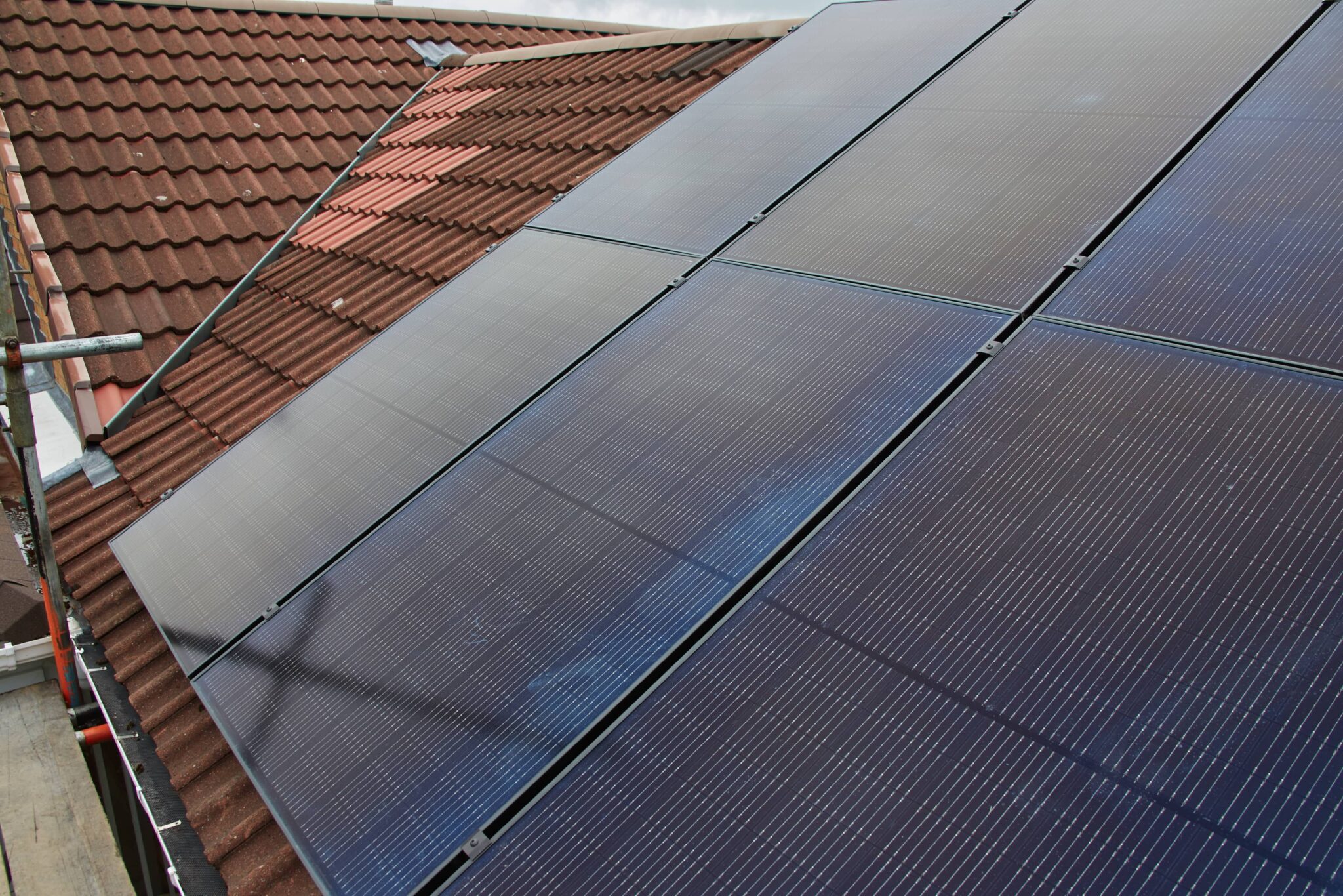 Solar panels mounted on the roof of a home next to traditional terracotta tiles.