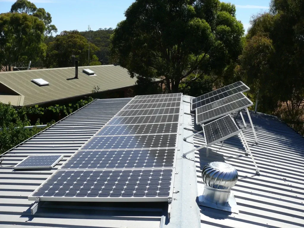 Solar panels installed on a retail business's metal roof surrounded by trees under a clear sky.